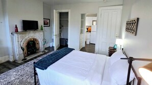 A bedroom with a bed, a fireplace, a television, and a hallway leading to a kitchen. - Cozy Studio in Allentown (Buffalo)
