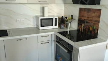 A modern kitchen with white cabinetry, a microwave, an oven, and a black range hood.