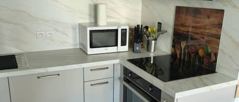 A modern kitchen with white cabinetry, a microwave, an oven, and a black range hood.