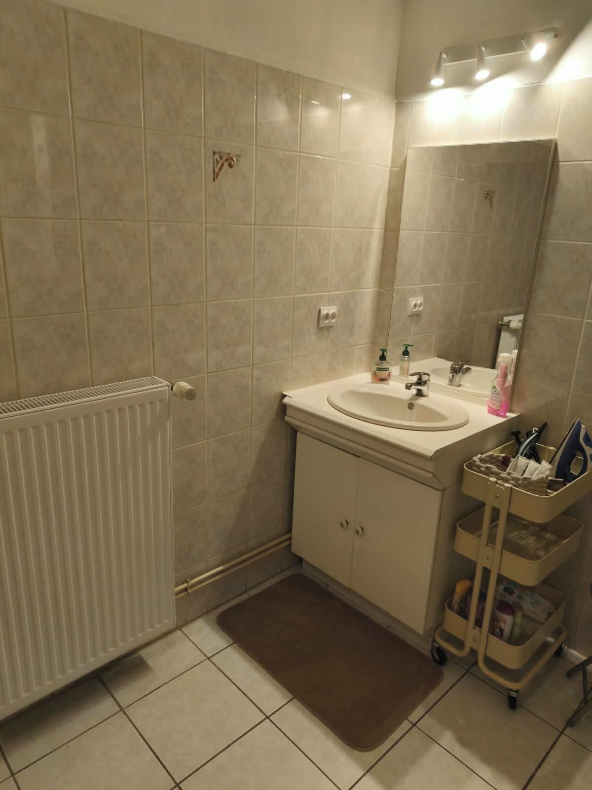 Ein Badezimmer mit einem weißen Waschbecken, einem Spiegel, einem Handtuchhalter und einer Heizung.