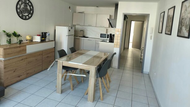 A modern kitchen with white cabinets, a wooden dining table, and a clock on the wall. - Vrbo Property (Château-Salins)