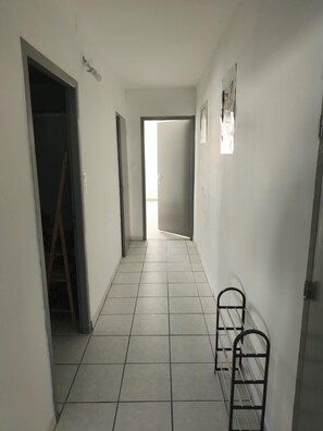 A hallway with tiled flooring, a metal rack, and a door leading to another room.