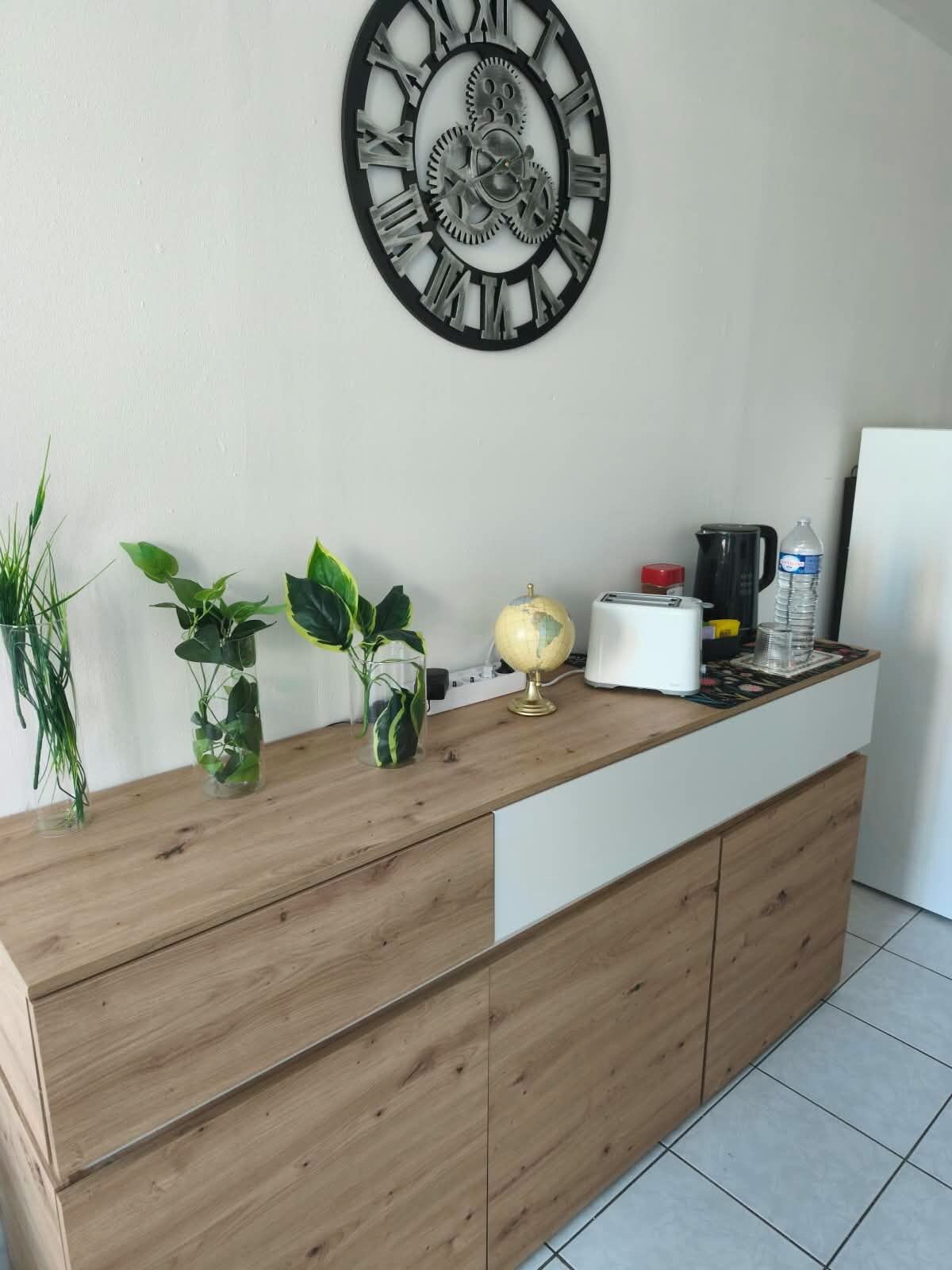 A kitchen counter with a clock, plants, a globe, and kitchen appliances.