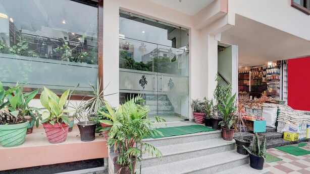 A building entrance with steps leading up to a glass door, surrounded by potted plants. - Super Collection O Vaishno Devi Temple (Katra)
