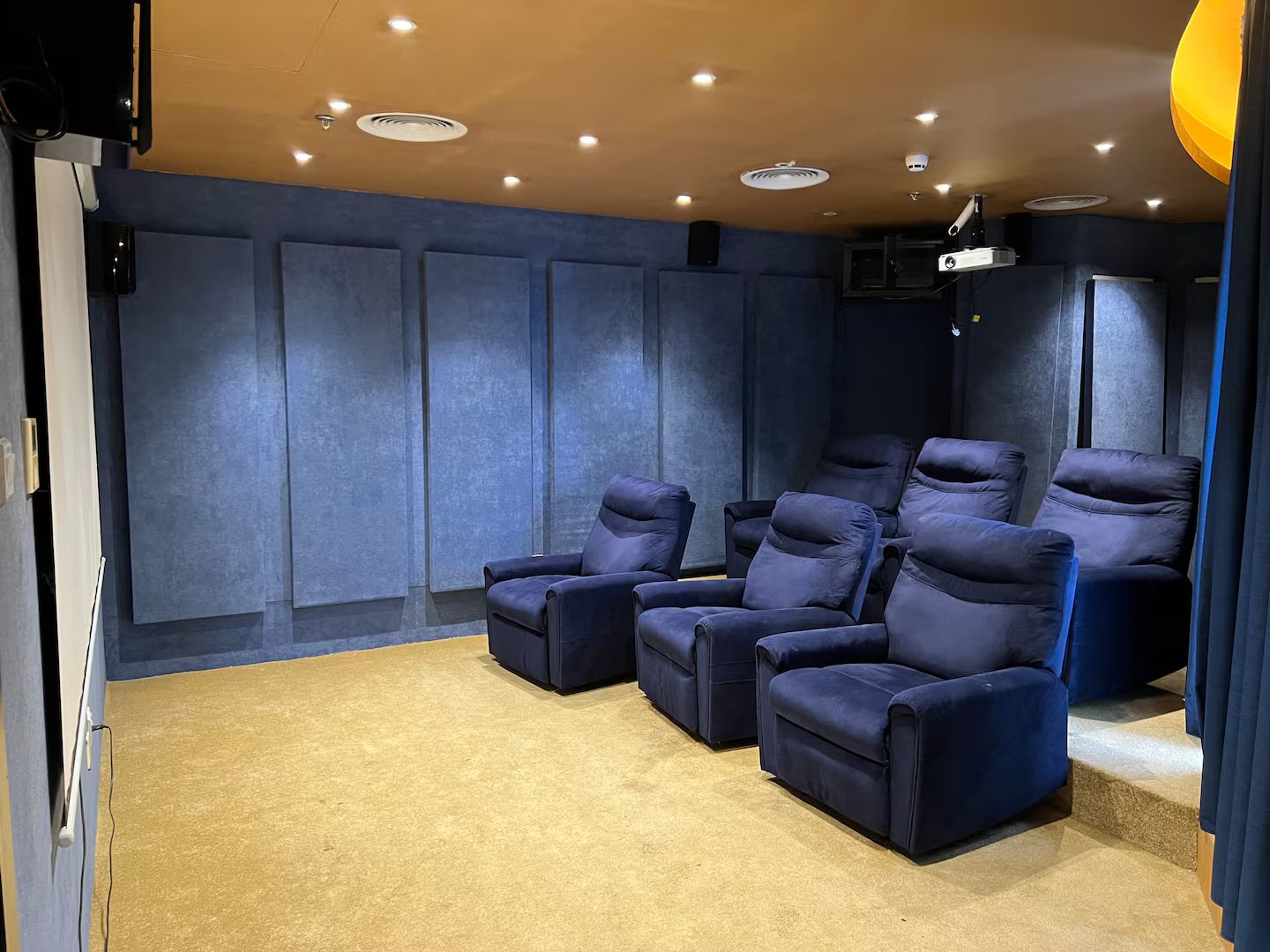 A home theater room with multiple dark blue reclining chairs, carpeted floor, and recessed ceiling lighting.