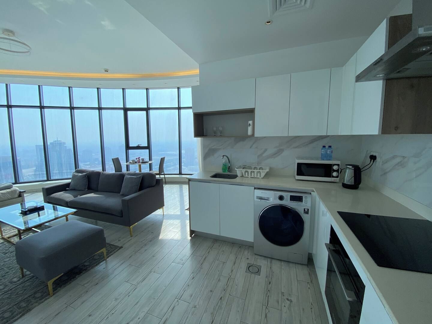 A modern apartment with a living area, kitchen, and large windows offering a city view.