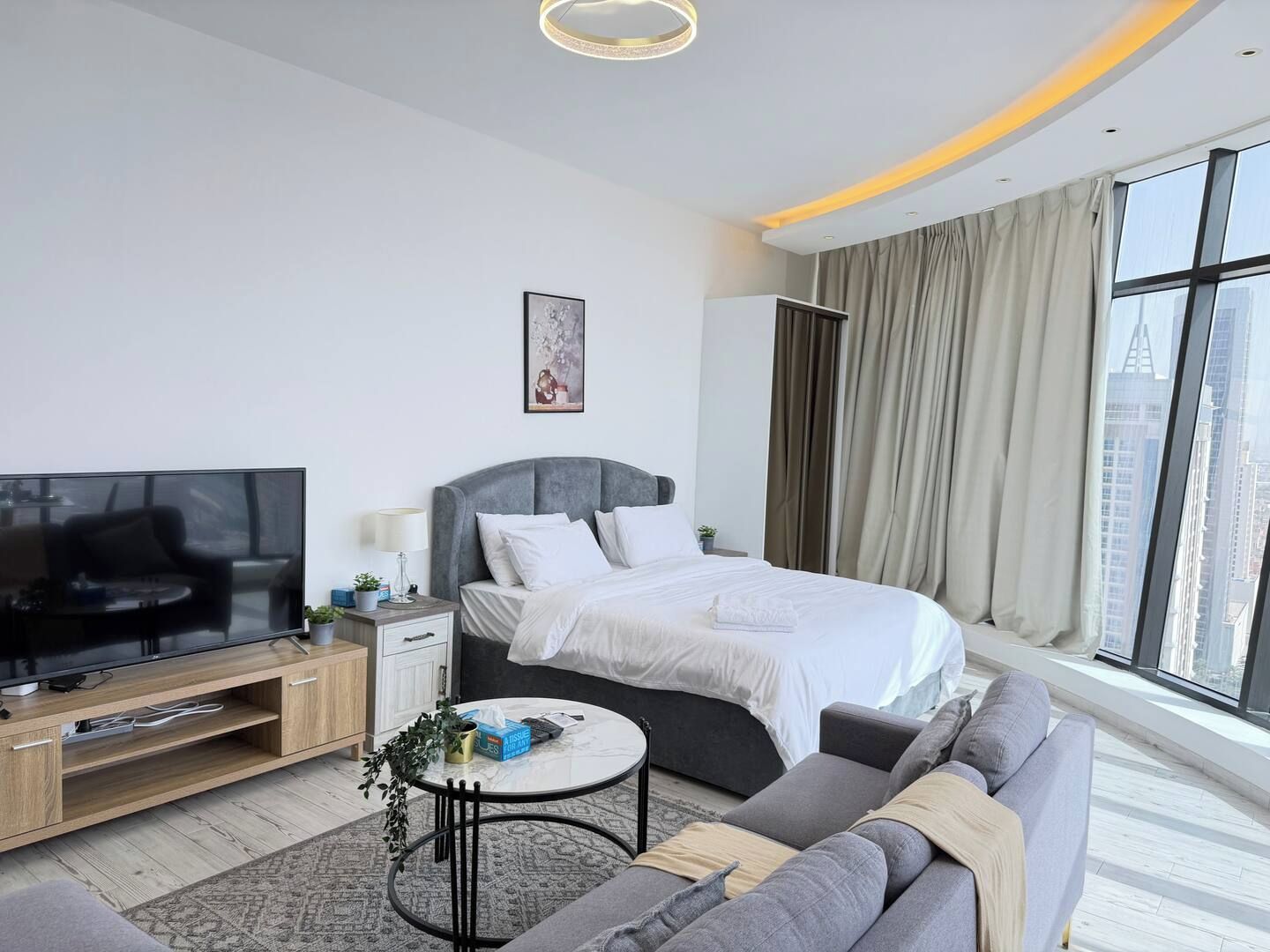 A modern hotel room with a bed, sofa, TV, and a city view.