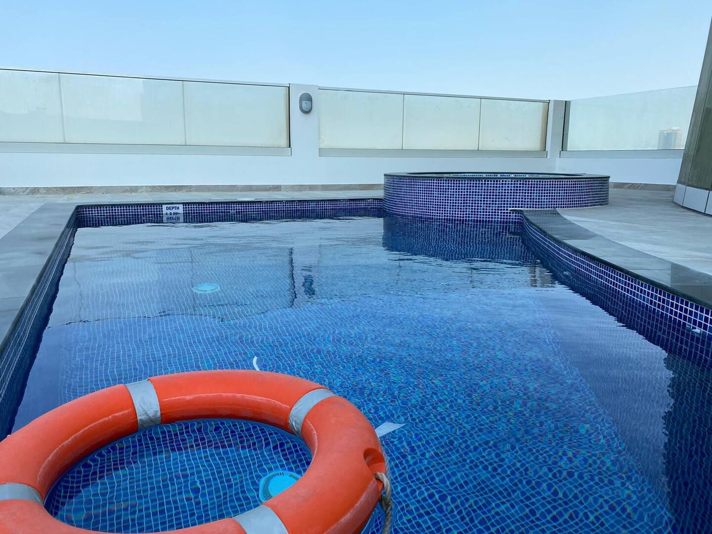 A rooftop swimming pool with a lifebuoy, clear blue water, and tiled edges.