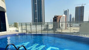 A rooftop swimming pool with a glass balustrade, surrounded by high-rise buildings. - Premium Escape with Panorama City View F281O (Seef)