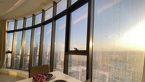 A dining area with a table set for two, large windows, and a view of a cityscape. - Premium Escape with Panorama City View F281O (Seef)