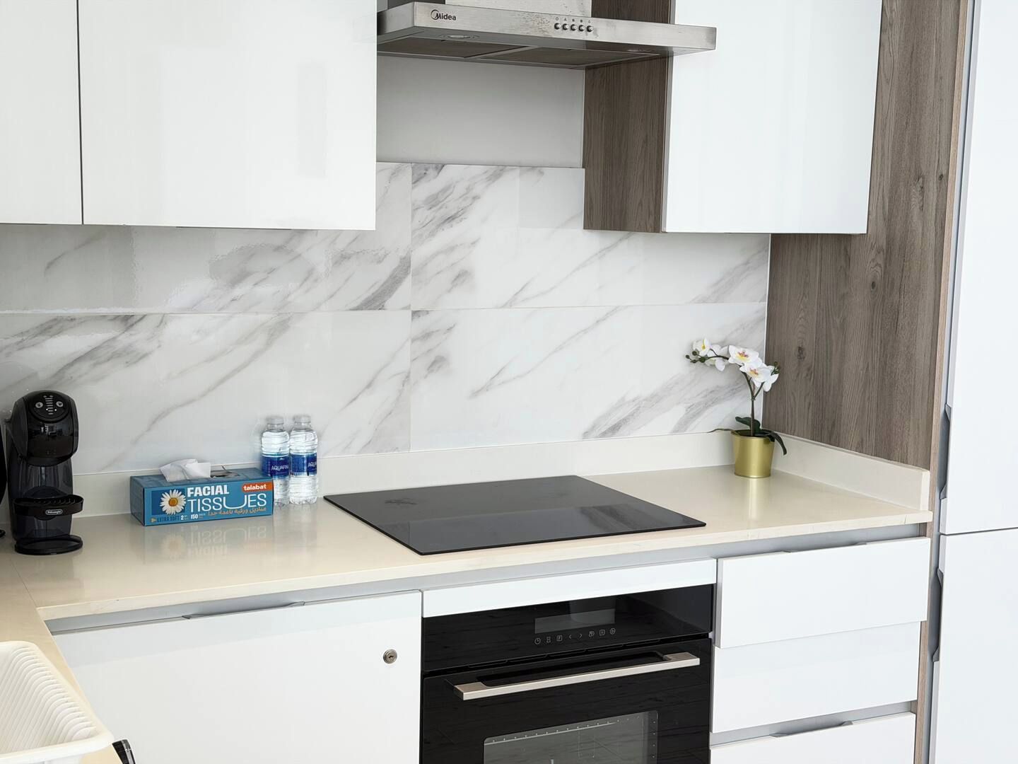 A modern kitchen with white cabinets, a marble backsplash, a coffee maker, facial tissue, and a potted orchid.