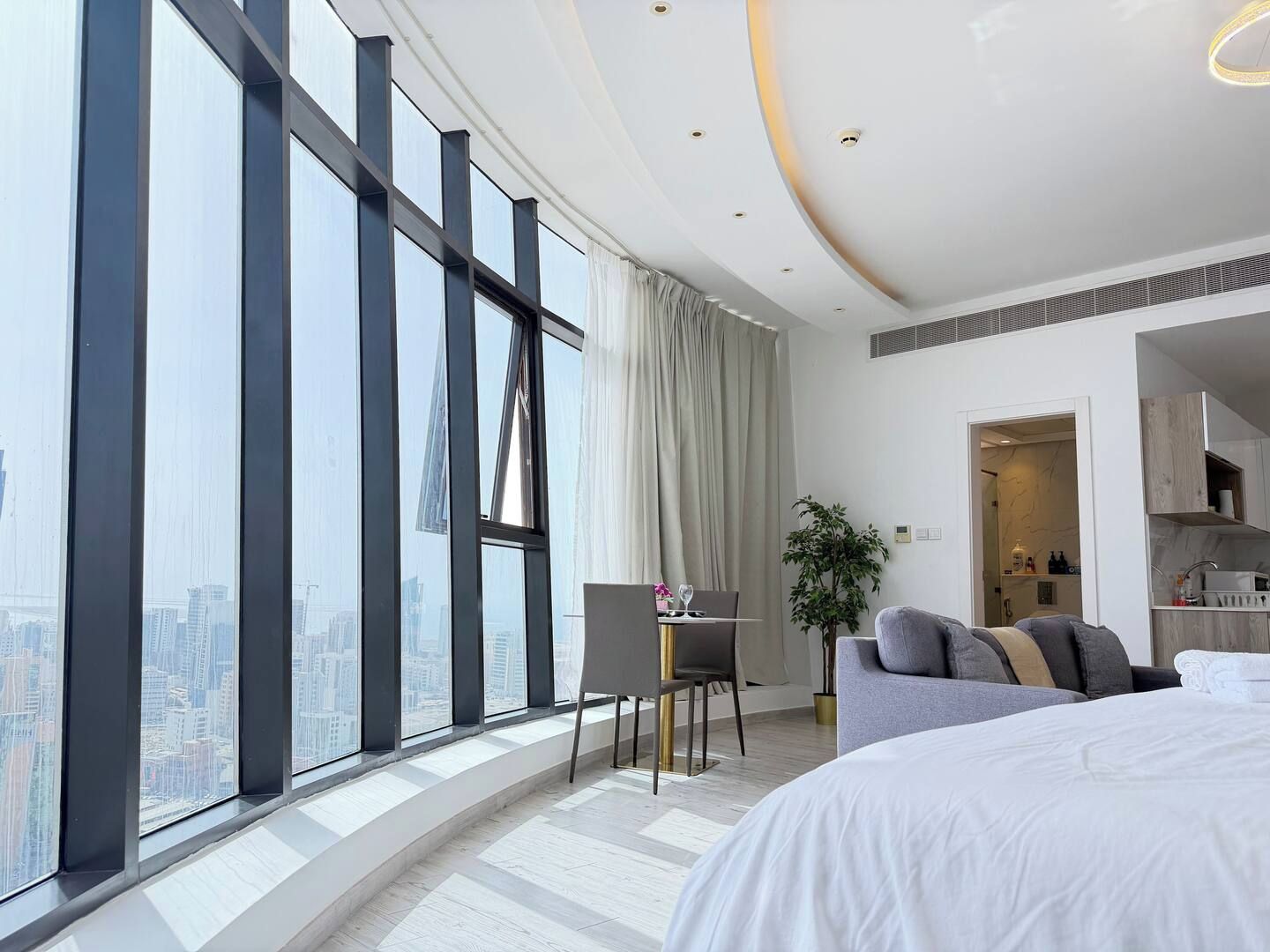 Una habitación de hotel moderna con un ventanal grande, cama, escritorio y kitchenette.