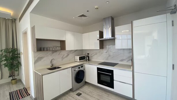 A modern kitchen with white cabinetry, a built-in washing machine, and a microwave. - Premium Escape with Panorama City View F281O (Seef)