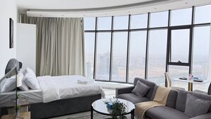 A modern hotel room with a bed, a sofa, a small table, and large windows offering a city view. - Premium Escape with Panorama City View F281O (Seef)