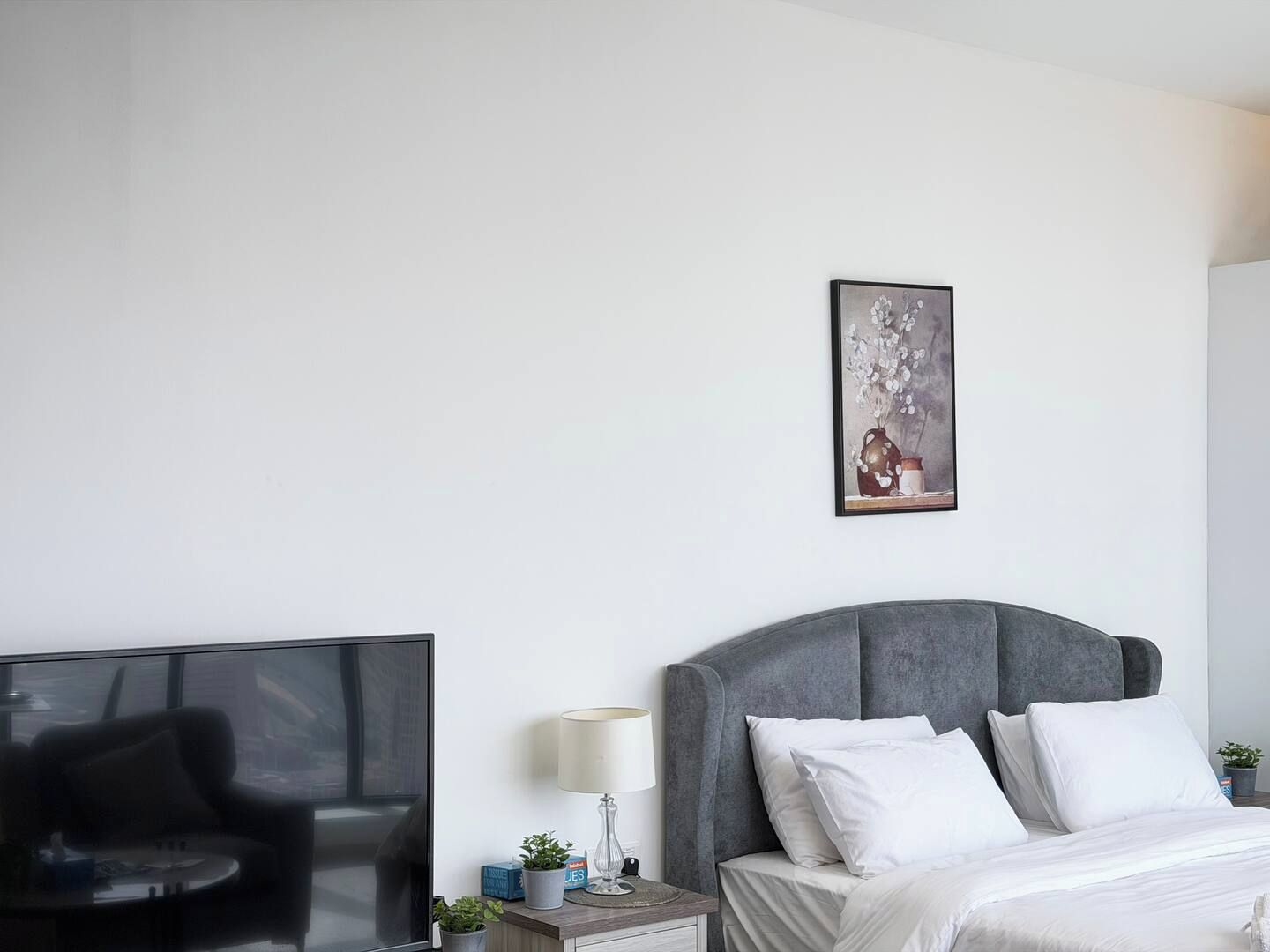 A modern hotel room with a bed, a TV, a desk, and a wall-mounted picture.