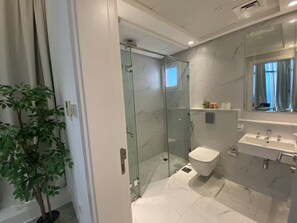 Et moderne badeværelse med et brusebadekar i glas, et hvidt toilet og en vask med marmor bordplade.