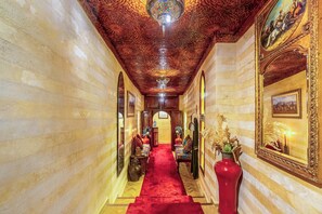 Um corredor com carpete vermelho, teto decorado e obras de arte emolduradas nas paredes.
