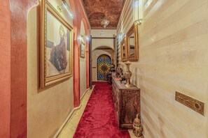 Corredor com carpete vermelho, obras de arte nas paredes e porta decorativa com vitral.
