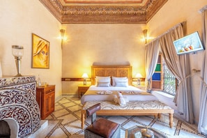 A hotel room with a large bed, a wooden nightstand, a wall-mounted TV, and a patterned floor. - Riad Rita Palace (Marrakech)