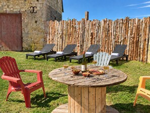 A patio with lounge chairs, a wooden table with food and drinks, and a bamboo fence. - Cottage de Perseigne (Barville)