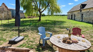 An outdoor dining area with a table set for two, surrounded by stone buildings and a large tree. - Cottage de Perseigne (Barville)