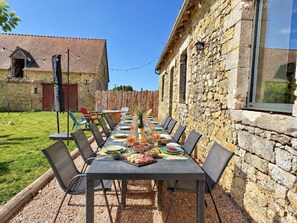 Een terras met een lange tafel gedekt voor een maaltijd, omringd door stenen muren en een houten hek.