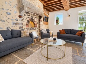 Un salon avec deux canapés gris, une table basse en verre et un mur en pierre agrémenté d’une arche en briques.