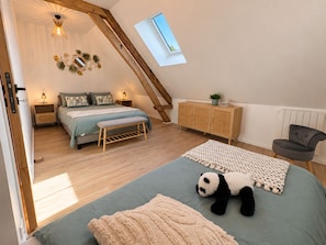 Ein Schlafzimmer mit schrägen Wänden, einem Bett, einer Bank, einem Nachttisch, einem Schrank, einem Stuhl, einem Fenster und einem Kuscheltier in Form eines Pandas.