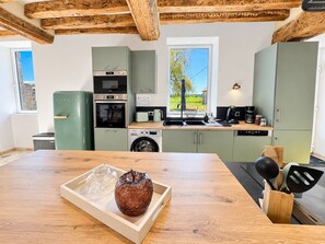 Une cuisine moderne avec une table en bois, un réfrigérateur vert, un four encastré et une fenêtre donnant sur un paysage verdoyant.