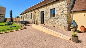 A stone building with a gravel driveway, outdoor seating, and a clear blue sky. - Cottage de Perseigne (Barville)