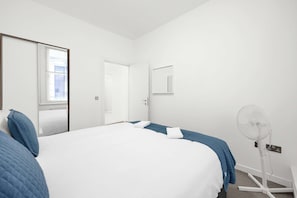 Quarto de hotel com cama grande, mesa de cabeceira, espelho, janela e ventoinha.