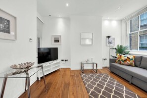 Een moderne woonkamer met een flatscreen televisie, een bank, een salontafel en een vloerkleed met een patroon.