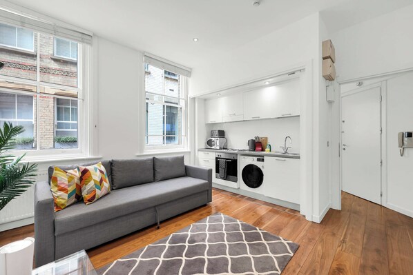 Un appartamento moderno con un divano grigio, una cucina completa di lavatrice e vista sulla città.