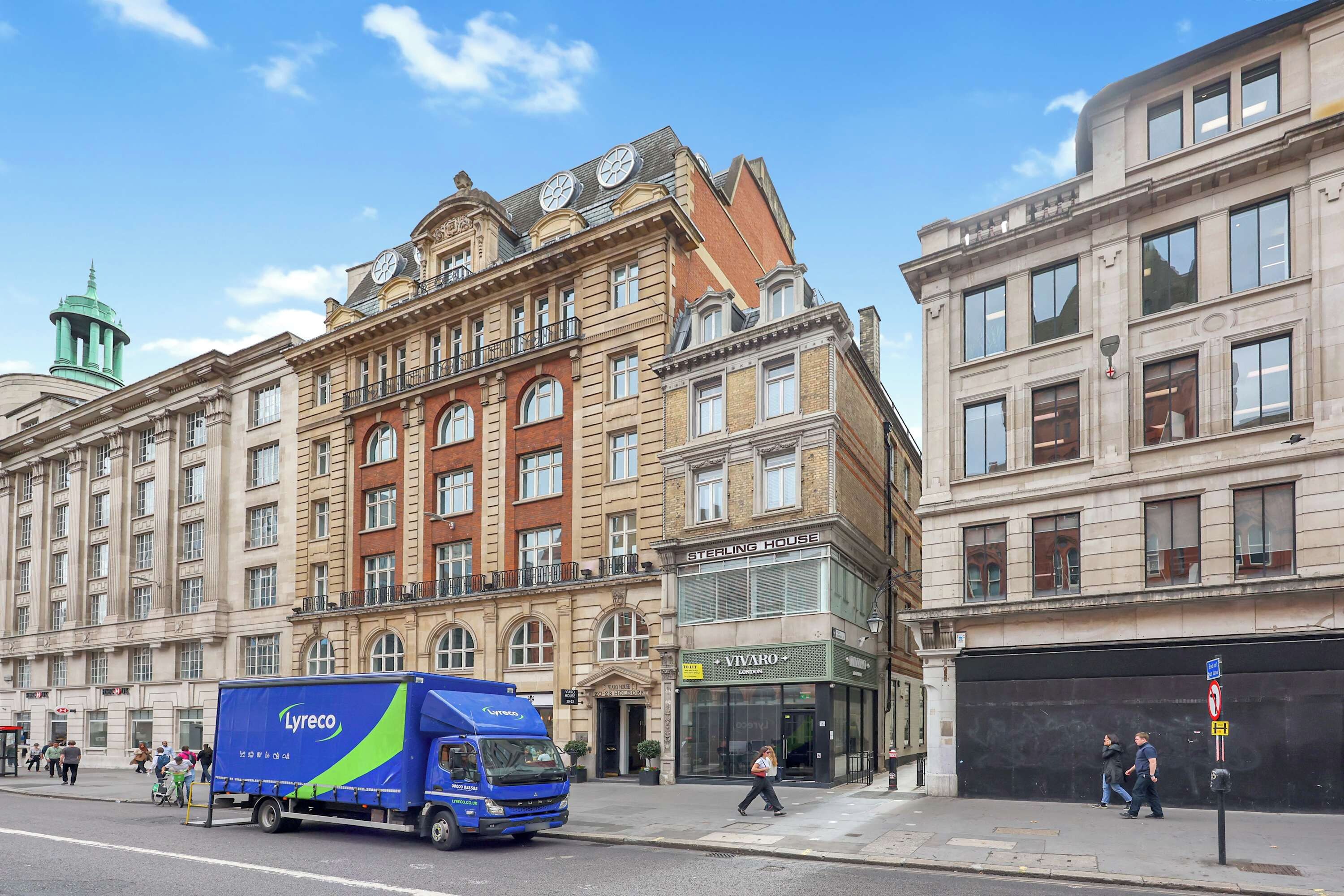 A street view with a blue delivery truck parked on the side of the road, a building with a sign reading 'Sterling House', and a pedestrian crossing the street.