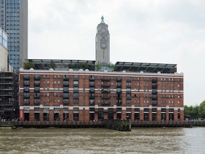 A multi-story building with a clock tower, a river in front, and a bridge with people. - 3SH one bed flat sleeps 4 in Holborn (Greater London)
