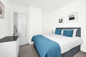 A hotel room with a bed, a desk, a chair, a fan, and two framed pictures on the wall. - 3SH one bed flat sleeps 4 in Holborn (Greater London)
