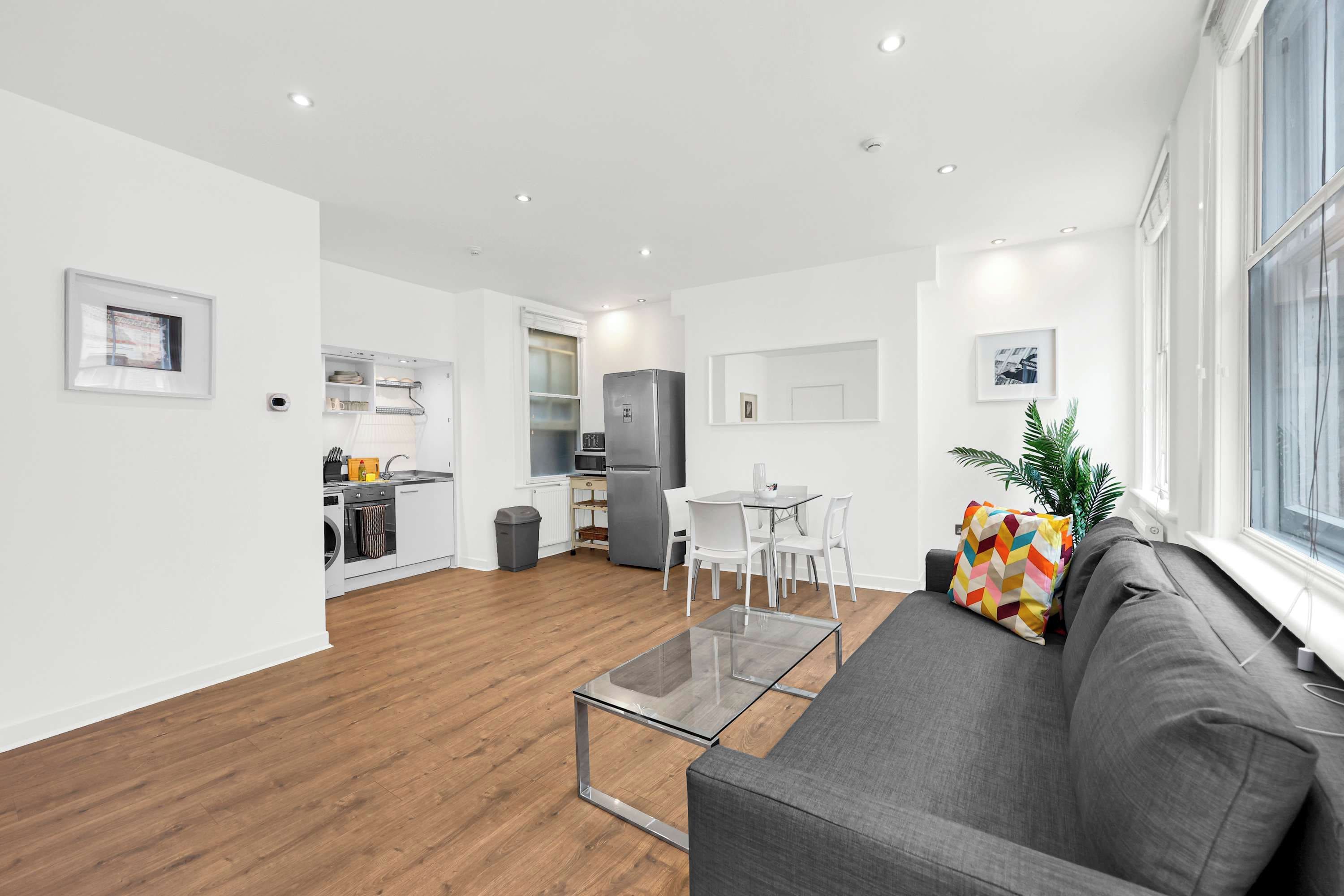 A modern living room with a grey sofa, a glass coffee table, and a dining area with white chairs.