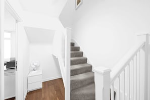 A staircase with a handrail, a landing with a white nightstand and a fan, and a wooden floor. - 6SH  one bed in Holborn sleeps 2 (London)