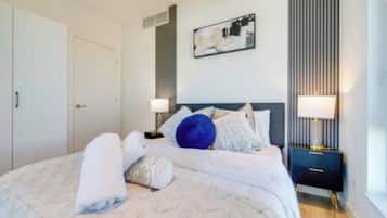 A neatly made bed with pillows and a rolled towel, a bedside table with a lamp, and a wall-mounted artwork.