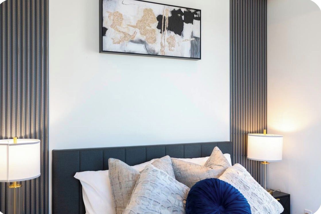 Una camera d'albergo con un letto, due lampade ai comodini e un quadro astratto appeso al muro.