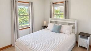 Quarto com cama grande, duas mesinhas de cabeceira, um criado-mudo e janela com cortinas.