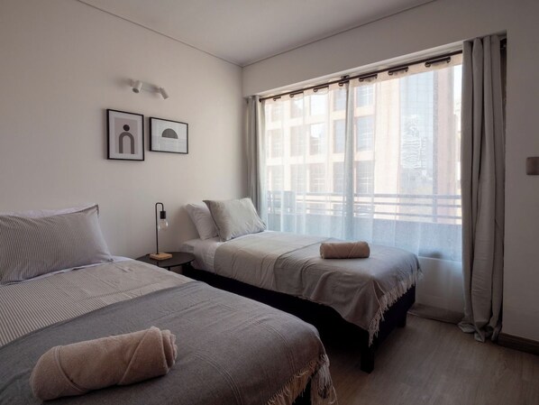 Une chambre d’hôtel avec deux lits, une table de chevet, une lampe et une fenêtre avec des rideaux.