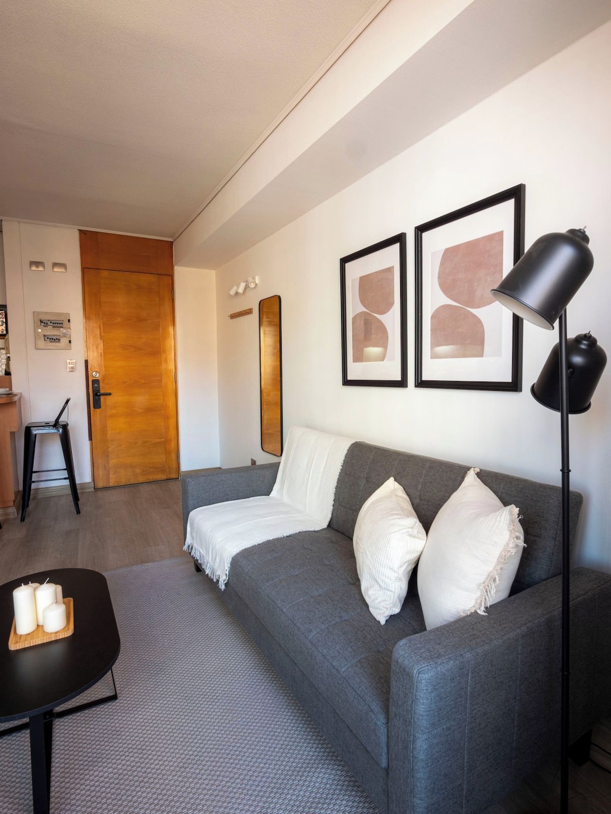 Ein modernes Wohnzimmer mit einem grauen Sofa, einer schwarzen Stehlampe und abstrakten Kunstwerken in Bilderrahmen an der Wand.