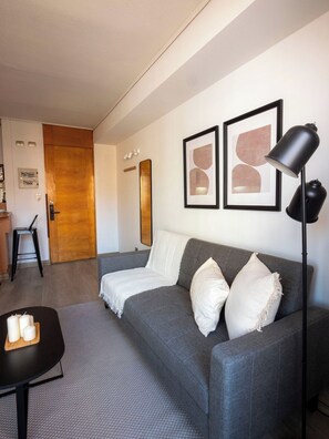 Un salon moderne avec un canapé gris, un lampadaire noir et des œuvres d’art abstraites encadrées accrochées au mur.