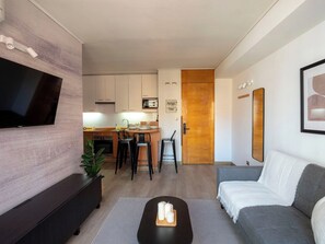 Un salon moderne avec un téléviseur à écran plat, un canapé gris et une table basse décorée de bougies.