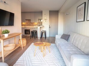 A modern living room with a white sofa, a wooden coffee table, and a TV mounted on the wall. - Costa Home - MUT Costanera & WIFI & Moderno (Santiago)