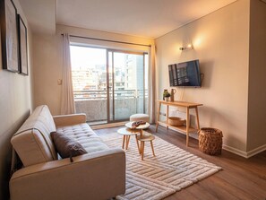 Un soggiorno moderno con un divano, un tavolino rotondo, una TV a parete e vista sulla città attraverso ampie finestre.