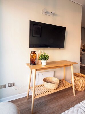 A modern living room with a flat-screen TV mounted on the wall, a wooden table with a plant, a vase, and a woven basket. - Costa Home - MUT Costanera & WIFI & Moderno (Santiago)
