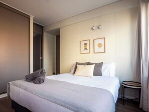 A hotel room with a bed, pillows, a small table, and a wall-mounted light fixture. - Costa Home - MUT Costanera & WIFI & Moderno (Santiago)