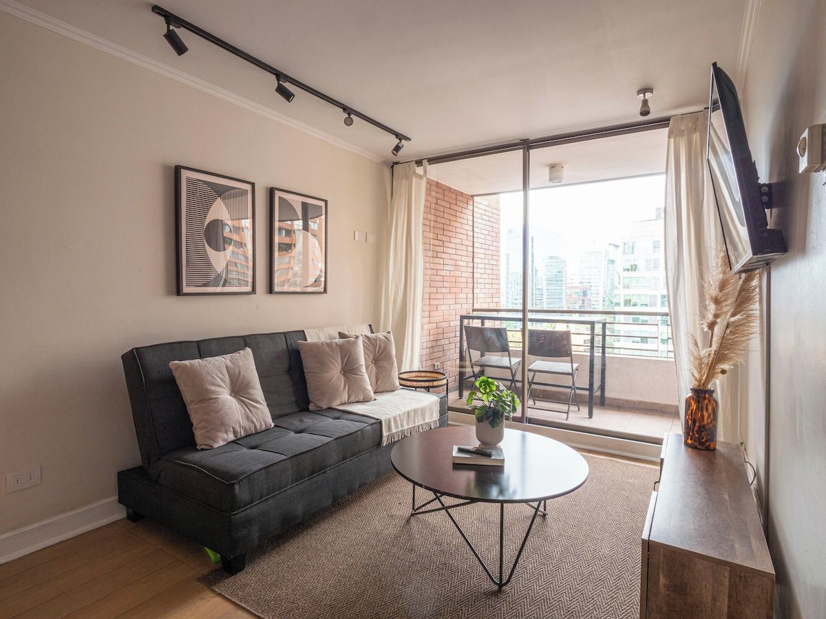 A modern living room with a sofa, a coffee table, and a view of the city through large windows.